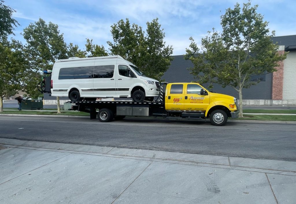 Professional towing service moving a white van on a flatbed truck.