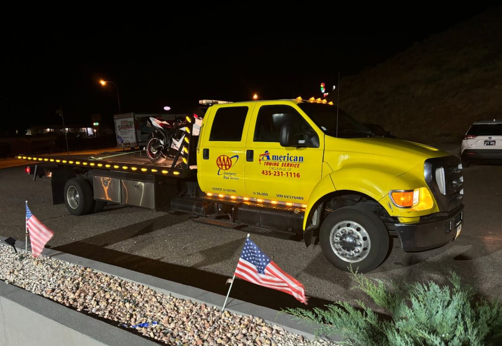 Yellow towing truck providing roadside assistance at night with American flags.