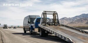 Blue towing truck carrying a silver van on a highway with mountains in the background